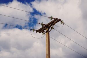 O poste de madeira com isoladores sustenta três fios, ilustrando soluções de energia, sob céu parcialmente nublado.