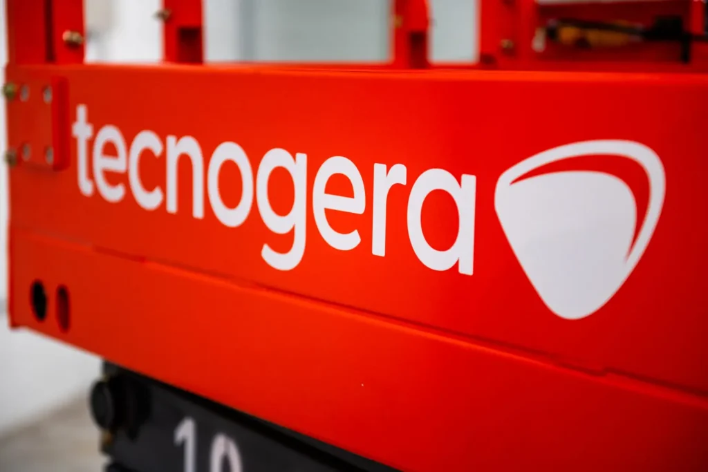 Close-up de uma máquina industrial vermelha, destacando o nome Tecnogera em branco e seu logotipo estilizado em formato de escudo. A imagem ressalta o compromisso da marca com energia em movimento, enquanto o fundo desfocado faz com que a atenção fique na cor vibrante e no visual da Tecnogera.