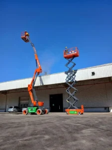 Na imagem, dois profissionais da Tecnogera usam EPIs e operam plataformas elevatórias laranja próximas a um prédio industrial.