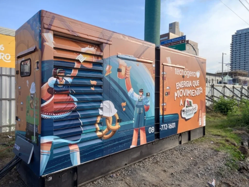 Gerador Tecnogera com ilustrações de trabalhadores e ferramentas, ao ar livre, frase "ENERGÍA QUE MUEVE" e cenário urbano no Oktoberfest Blumenau.