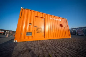 Gerador laranja da Tecnogera sobre paralelepípedos, céu azul ao fundo e ambiente industrial, pronto para soluções no Apagão.