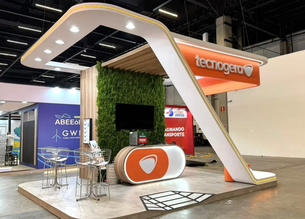 Stand da Tecnogera na Brazil Windpower 2025 com tons branco e laranja, estrutura arco, painel verde e balcão personalizado.