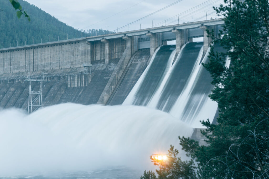 A barragem de concreto libera água por três vertedouros, ilustrando a energia hidrelétrica.
