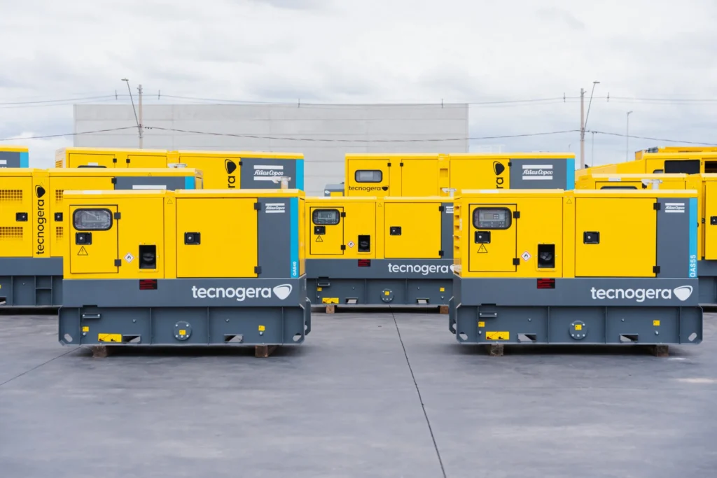 Grandes geradores amarelos Tecnogera ao ar livre, ideais para data centers e garantindo energia contínua, com prédio ao fundo.