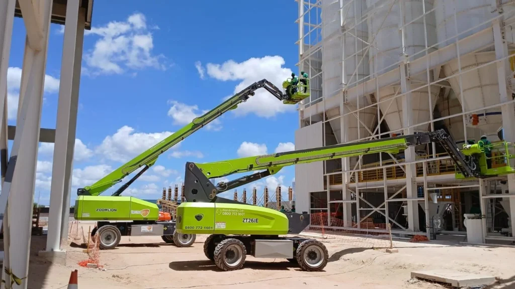 Na imagem, os equipamentos Tecnogera trabalham em altura junto a obra, com céu azul e materiais de construção ao redor.