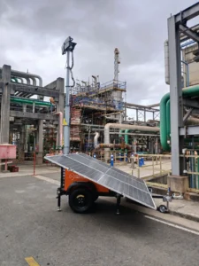 Unidade solar Tecnogera com antena e painéis ilumina obra noturna entre tubos e andaimes, sob céu nublado, com barreiras visíveis.