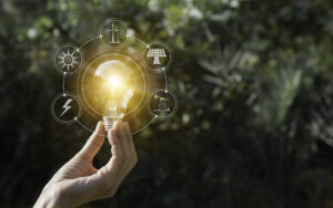Uma mão segura uma lâmpada acesa, com ícones de energia limpa ao redor, representando a transição energética.